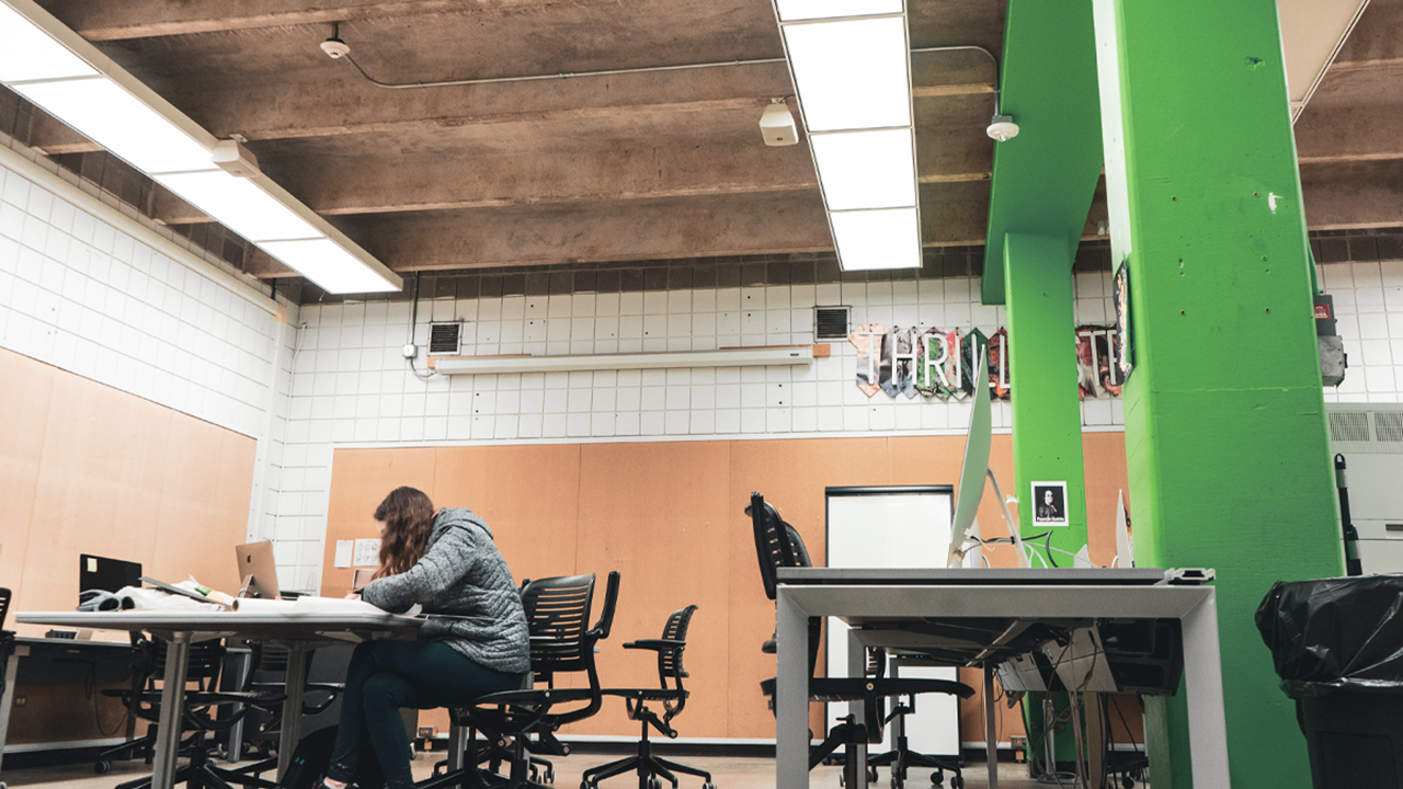 A photo of a classroom in the Fine Arts building. A student is sitting at a table working on a project.