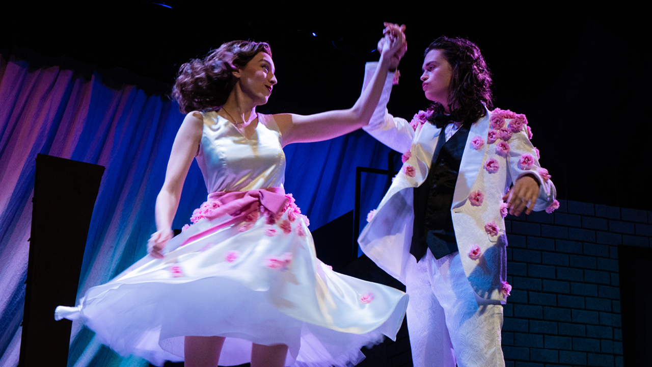 Two theatre students hold hands and dance. The student on the left twirls the student on the right.