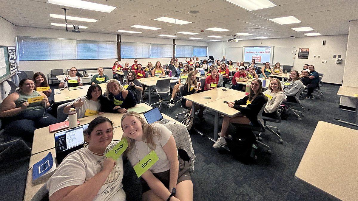 A group of teacher candidates pose for a photo in a large classroom.