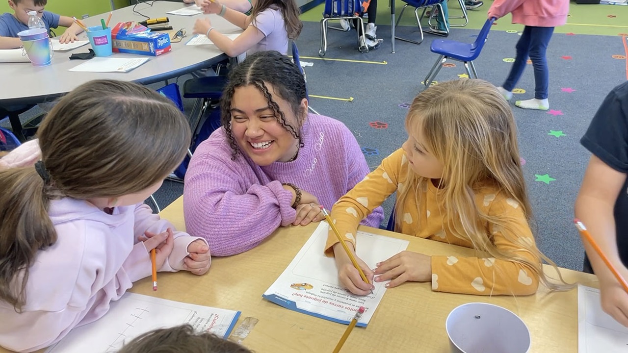 Ana Rodriguez Garcia sits with elementary students in a classroom.