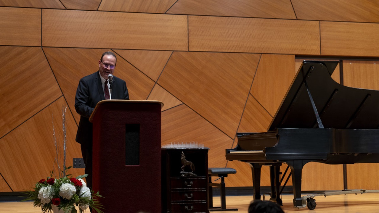 Bruce Kelley standing behind the podium on stage at the 2023 Celebration of Excellence event. He is talking to the audience. Bruce Kelley standing behind the podium on stage at the 2023 Celebration of Excellence event. He is talking to the audience.
