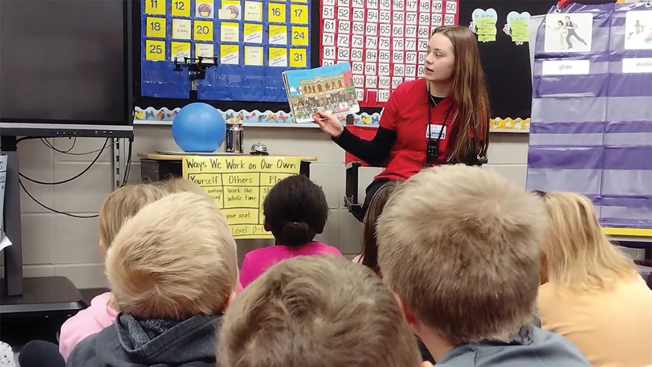 A Health Sciences student reads a book to children in a classroom.