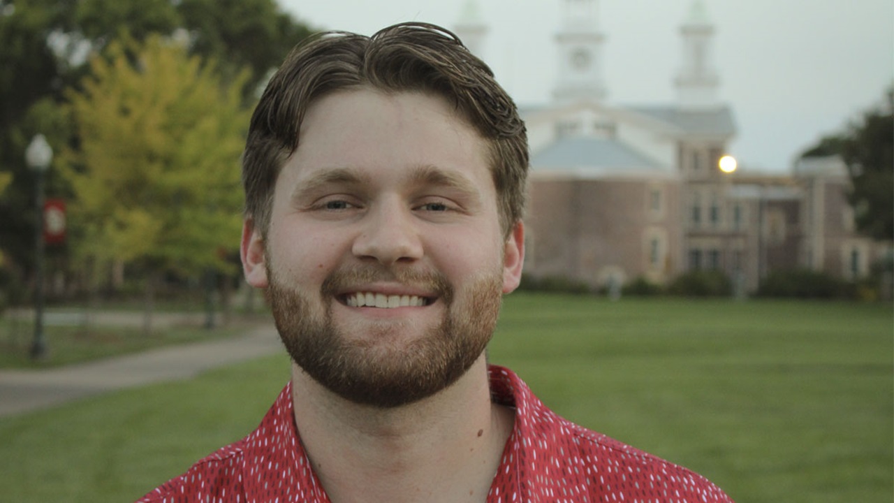 Ben Compton, wearing a red USD polo shirt, stands in front of Old Main. Ben Compton, wearing a red USD polo shirt, stands in front of Old Main.