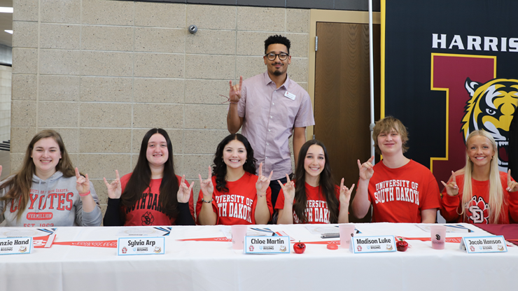School of Education Recruiter Dajshon Keel stands with future USD School of Education students, all wearing red shirts, at an Educators Rising signing day event.
