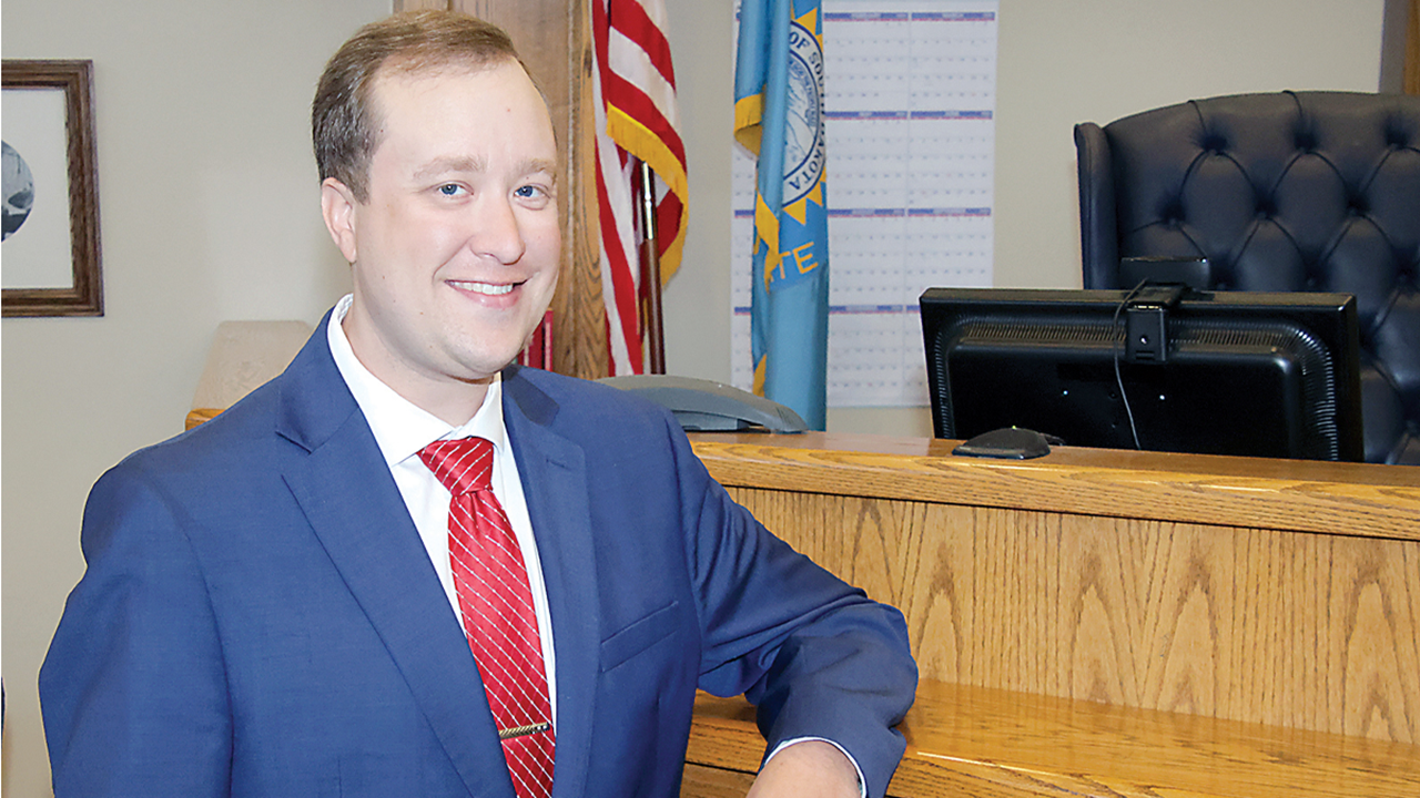 Tyler Larsen stands in a Yankton courtroom with his arm leaned against a wooden desk.