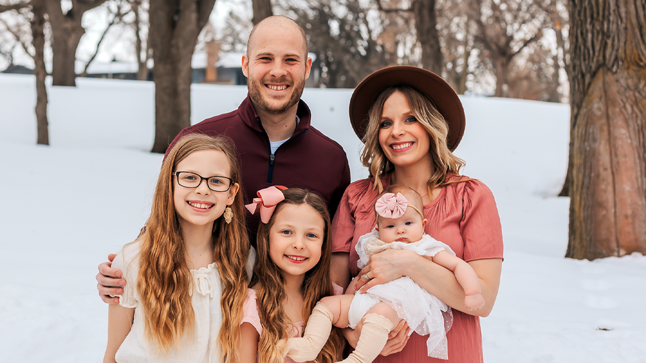 Chris Keyser stands with his wife and three daughters for a family photo. It's winter and there is snow behind the family.