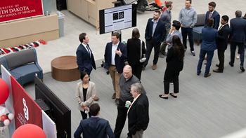 People in suits stand around and converse at a research symposium.