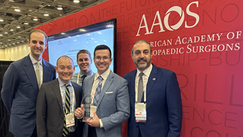 A group of medical professionals wearing suits holds a plaque and stands together in front of a red wall that has the words American Academy of Orthopaedic Surgeons on it.