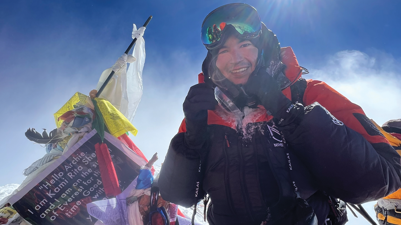 Dr. Jacob Weasel smiles on top of a mountain while wearing winter hiking gear.