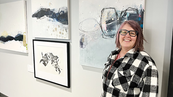 Mary Zajicek stands proudly next to her artwork, which is installed on a white wall at Bancorp in Sioux Falls.