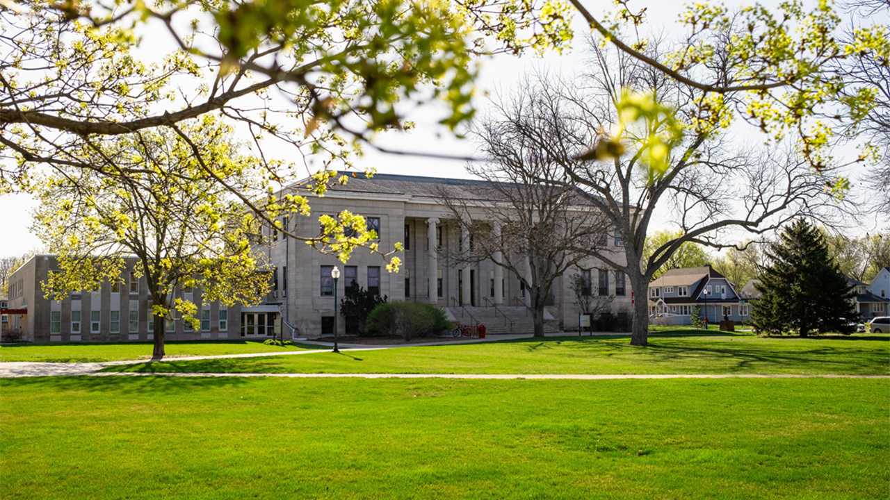 The College of Arts & Sciences exterior, with a sunny, green campus surrounding it.