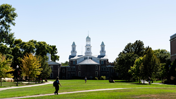 Students walk across the USD campus, with Old Main in the background.