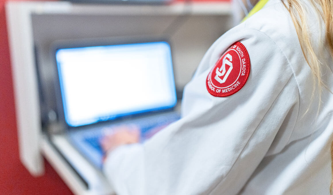 A physician within the Sanford School of Medicine wears her white coat and works in front of a computer.