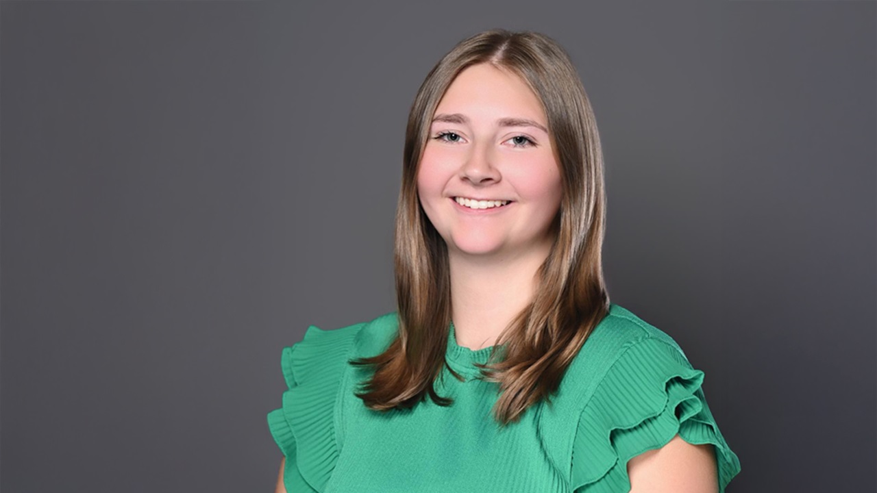 Rachel Stuckenbroker wears a green shirt and poses for her professional headshot against a dark gray background.