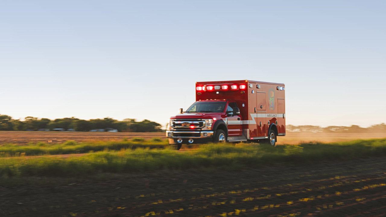 An red and white ambulance speeds down a dirt road.