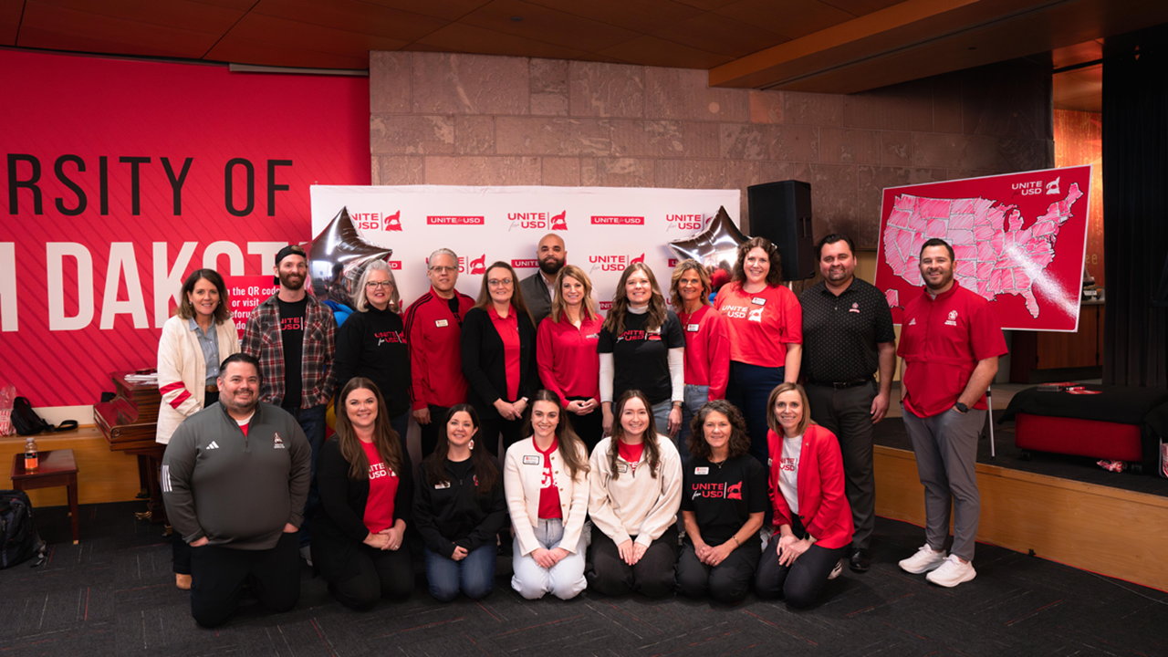 Unite for USD staff pose for a picture in front of a Unite for USD banner.