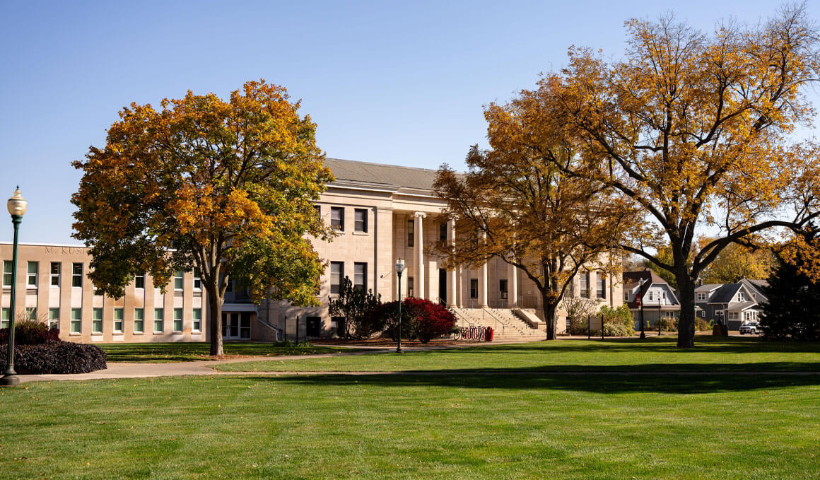 The College of Arts & Sciences sits on a sunny USD campus, surrounded by fall trees and fallen leaves.
