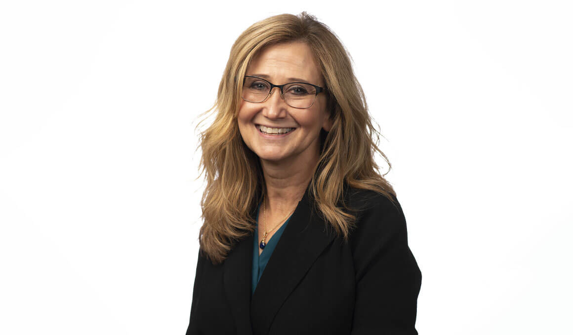 Michelle Baack, M.D., poses for her professional photo against a white backdrop. She is wearing a black blazer, glasses and smiling at the camera.