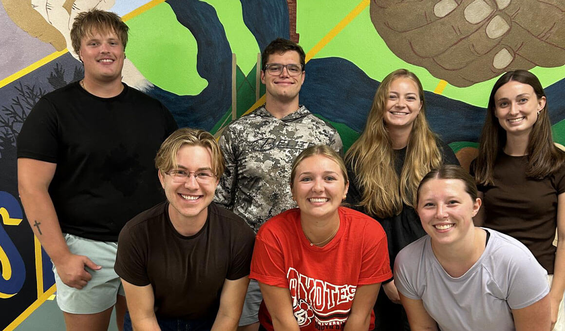 USD Sanford School of Medicine students stand in front of a colorful mural at one of their places of volunteer with the USD Office of Service Learning and Community Engagement.