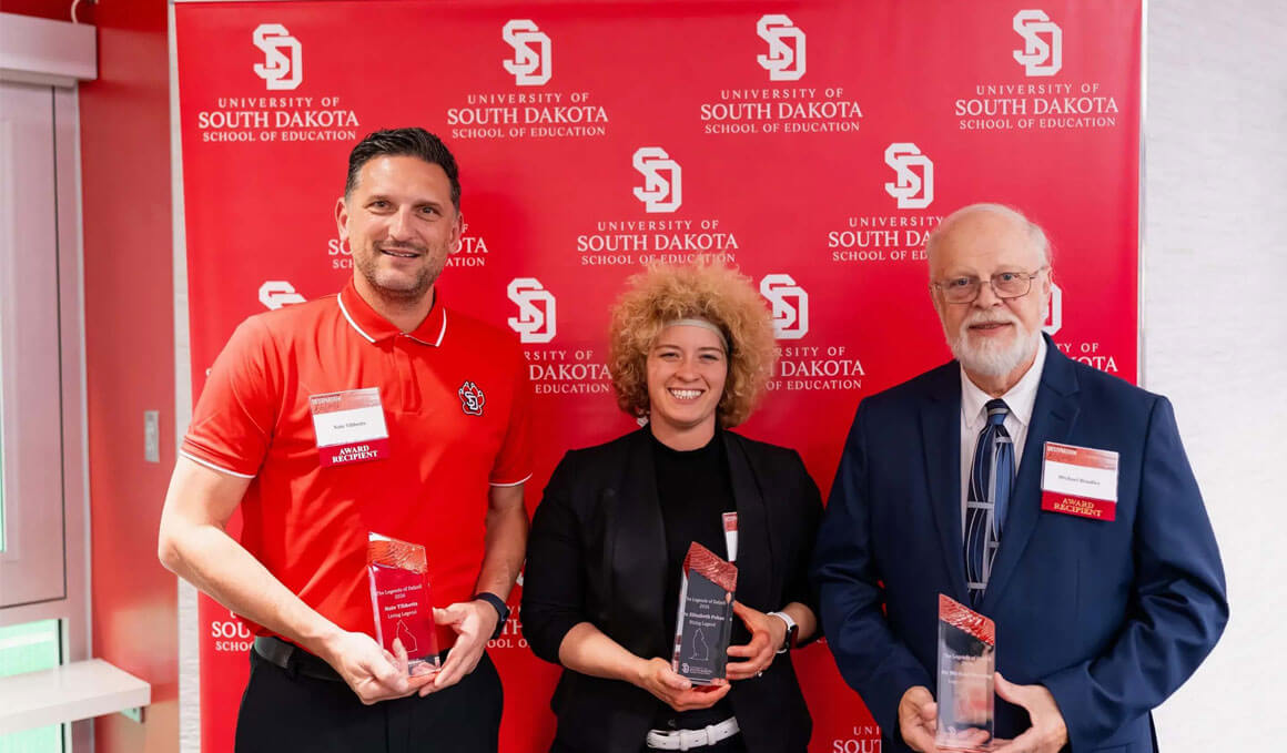 Recipients of the USD Legends of Delzell Awards stand in front of a USD branded backdrop. They are dressed in professional attire, smiling and holding their awards.