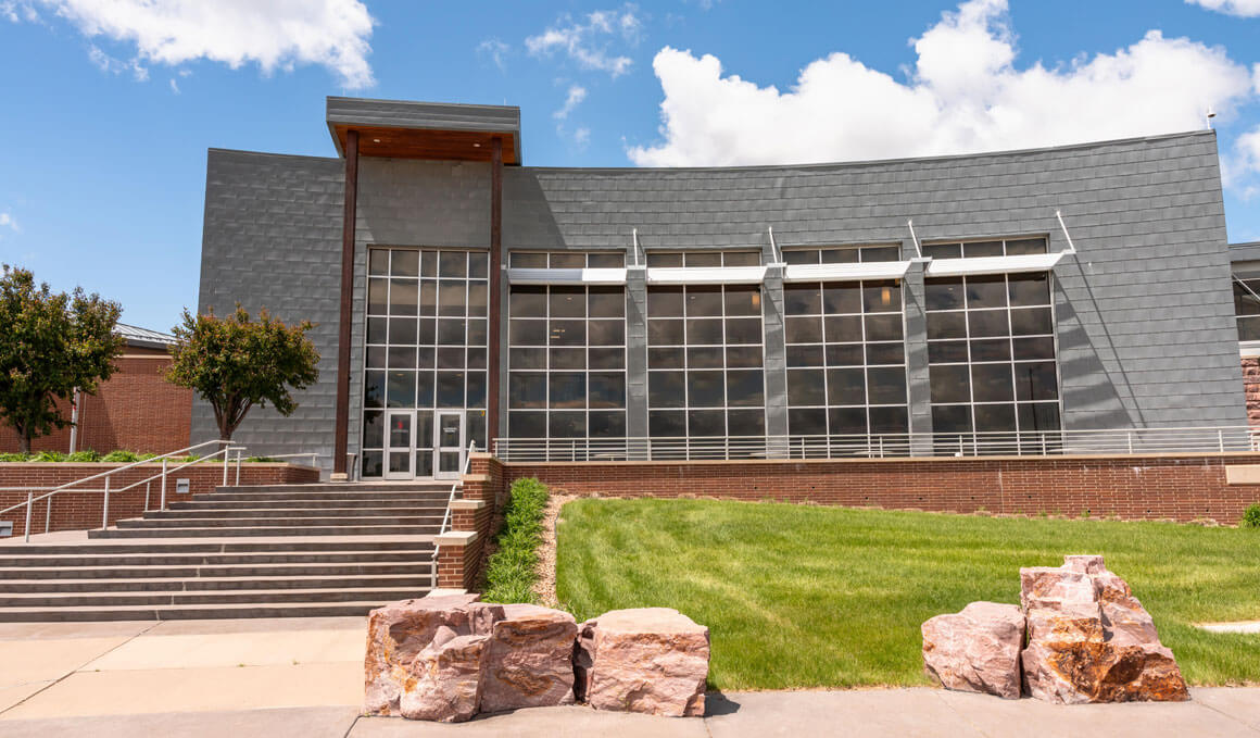 The Classroom Building sits on the USD – Sioux Falls campus, with a blue sky in the background and stars, boulders and green grass in the foreground. 