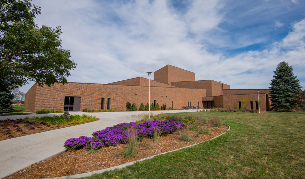 An exterior photo of the Warren M. Lee Center for the Fine Arts, with purple flowers in the foreground.