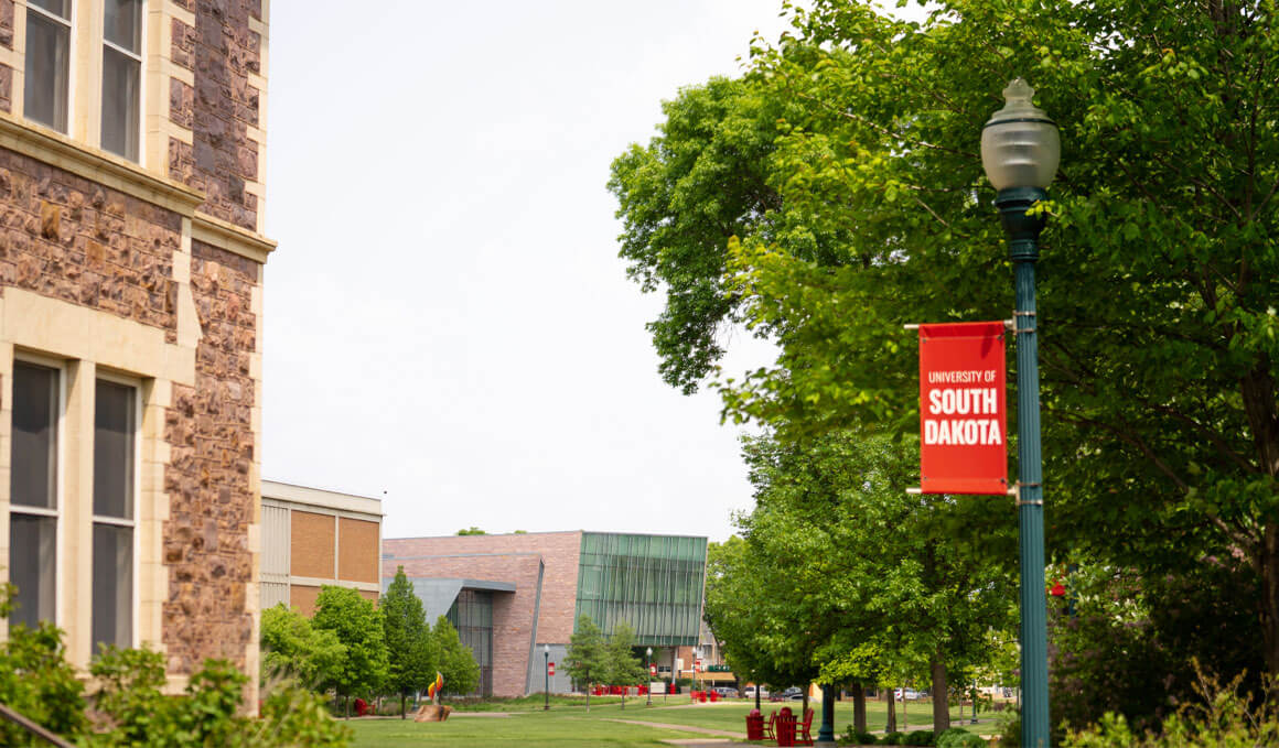 A view of the USD campus, including a corner of Old Main, the MUC and a light pole with a USD banner.