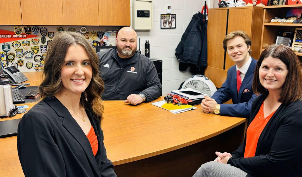 Bryant Jackson sits in an office with other USD colleagues. They are smiling at the camera.