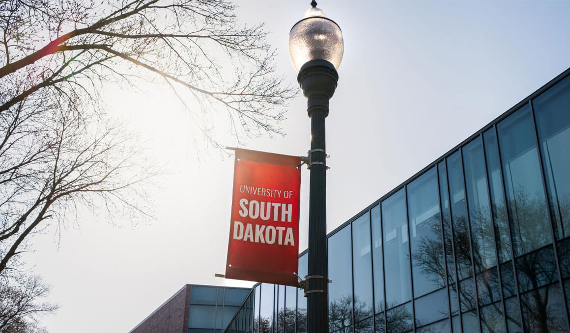 A red, USD banner is attached to a lightpole, with the MUC in the background and bare tree limbs in the background.