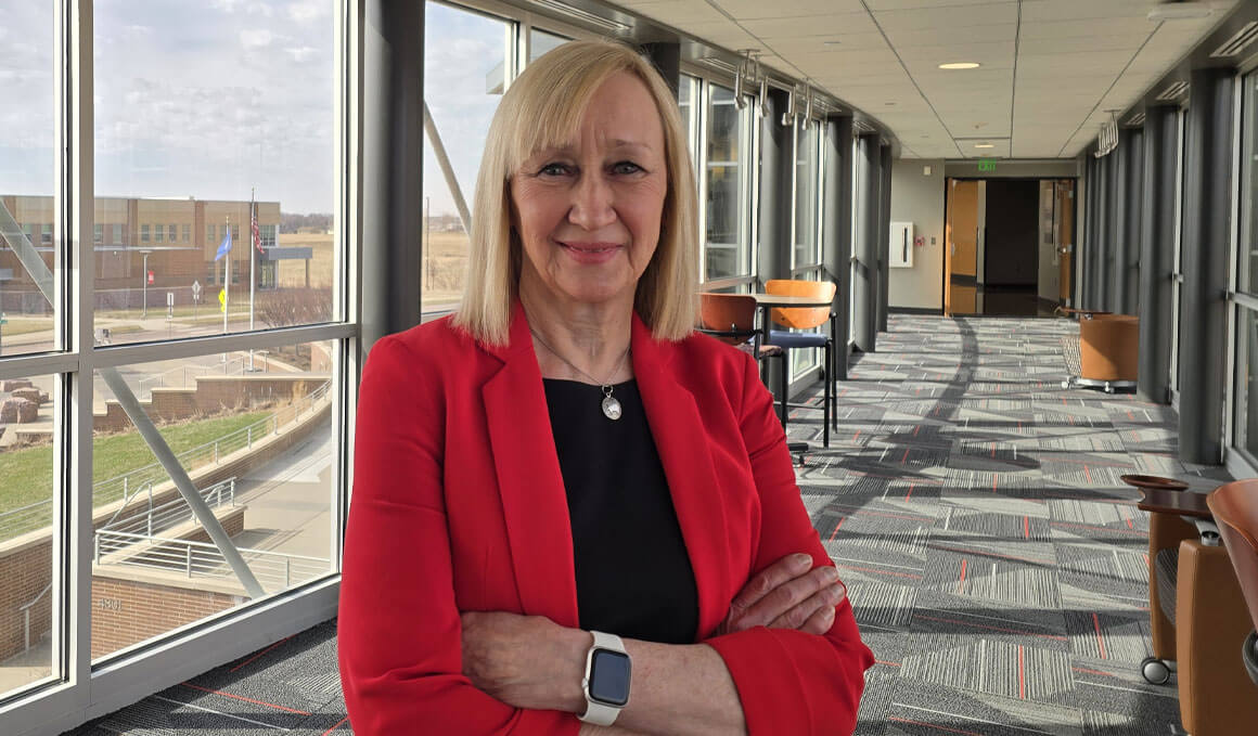Cheryl Hartman stands in a hallway at USD – Sioux Falls. She is smiling at the camera.