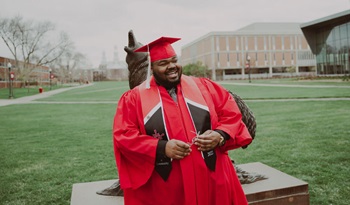 Marcus Destin stands in his graduation regalia in front of the Coyote Legacy statue on the USD campus in Vermillion.
