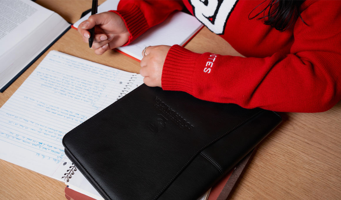 A Knudson School of Law student sits at a table, with notes displayed in front of her, as she studies a case. There is also a black binder on the table, with "The University of South Dakota" inscribed on it.