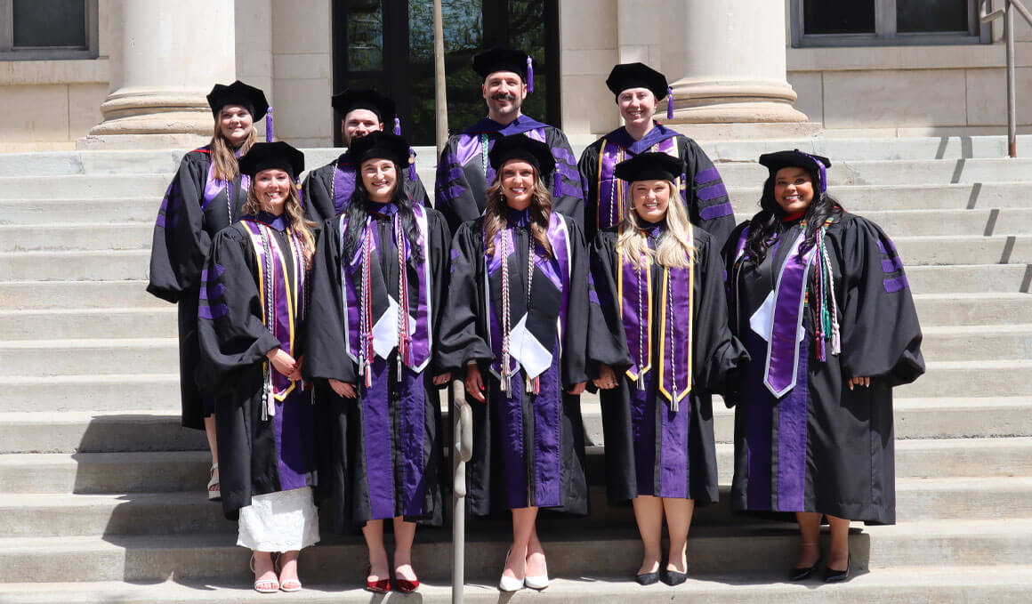 Public Service Pathway graduates stand on steps in their graduation regalia, smiling and posing for a picture.