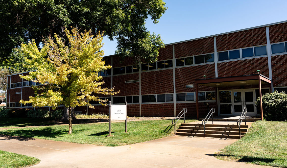 The Delzell Education Center, home to USD's School of Education, sits on a sunny campus, surrounded by green grass, trees and a blue sky.