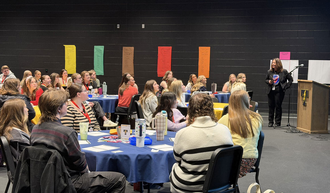 A speaker stands at a podium addressing teacher candidates, who are seated at round tables during a informational session at the Tea Area School District internship.