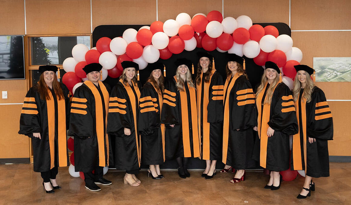 USD DNAP students stand smiling in their black and orange regalia, with red and white balloons behind them.