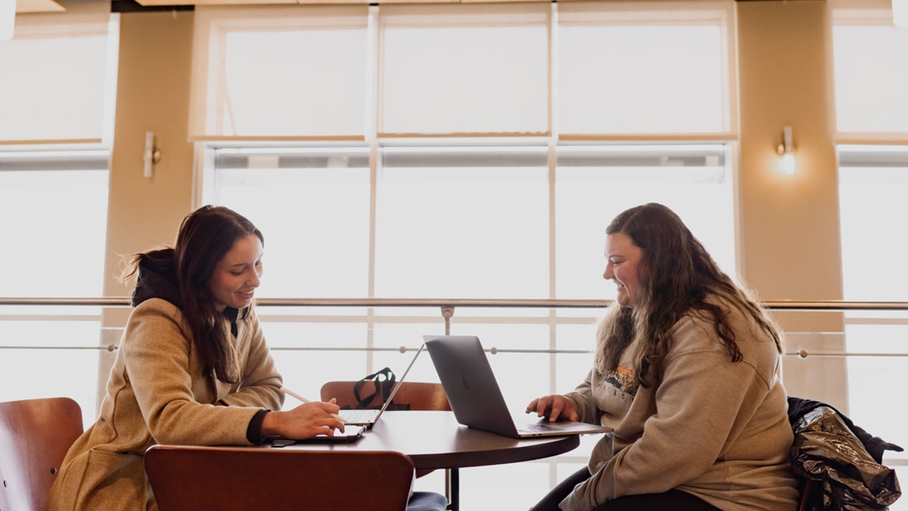 Two students sitting at table studying in front of window