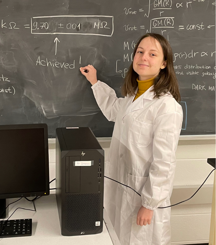 Oleksandra "Sasha" Lukina smiling and writing an equation on a chalkbord in a lab.