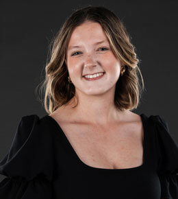 Cloie Stevens poses for her professional photo against a dark background. She is wearing a black dress and smiling at the camera.