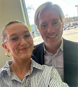 Katie Gellerman stands in front of a window with her mentor Eric Siversten, CEO of Epicosity, as they both smile at the camera.