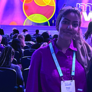 Sheyma Musterih Abdikebir stands in the conference in front of TV screens.