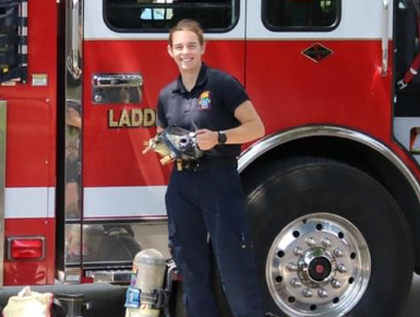 Lilly McNaughton stands in front of a firetruck in her EMT uniform. 