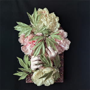 A sculpture of hands holding flowers that are white and pink, with green leafs. This sculpture is part of the, "In Her Material Realm," a solo exhibition of installation and other recent works by Susan M. Heggestad, ’99.
