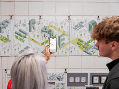 Professor Kim stands in front of a poster, with a cell phone in her hand, and shows a student the cell phone.