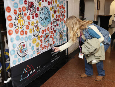 A person is interacting with a large display board that says "Careers in the Arts," which is covered in stickers and/or small artworks.
