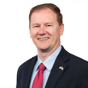 A headshot of Joe Kippley wearing a navy suit and red tie.