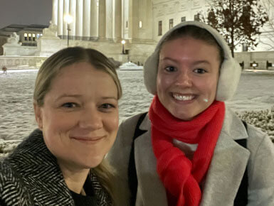 Two USD Knudson School of Law students are dressed in winter gear, posing for a photo in front of a building in Washington D.C.
