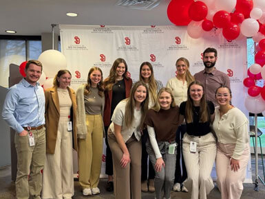 USD SSOM students stand in front of a USD backdrop, posing for a group picture at the Coyote Clinic.