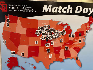 A map of the United States sits on an easel, with polaroid picture pins stuck in the map, corresponding to the locations that USD SSOM students matched with.