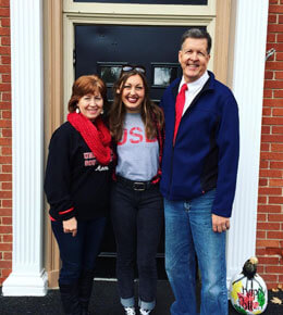 Paige Wright stands with her parents for a photo in front of a door. They are all smiling at the camera.
